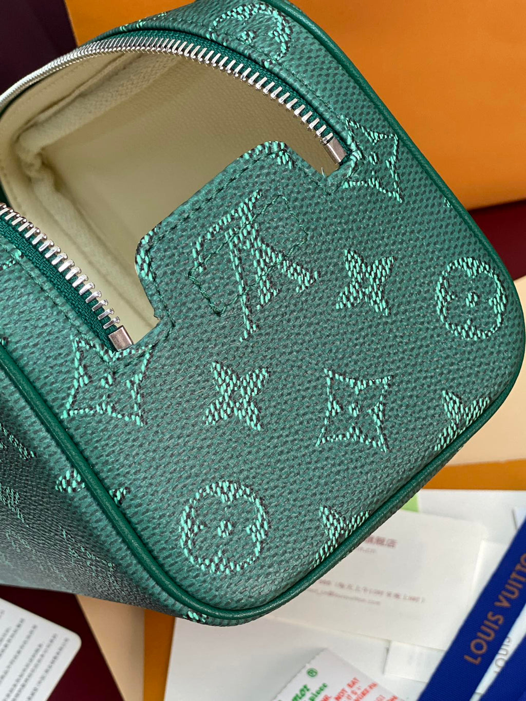 Green monogram bag opening with beige lining and zipper closure visible.