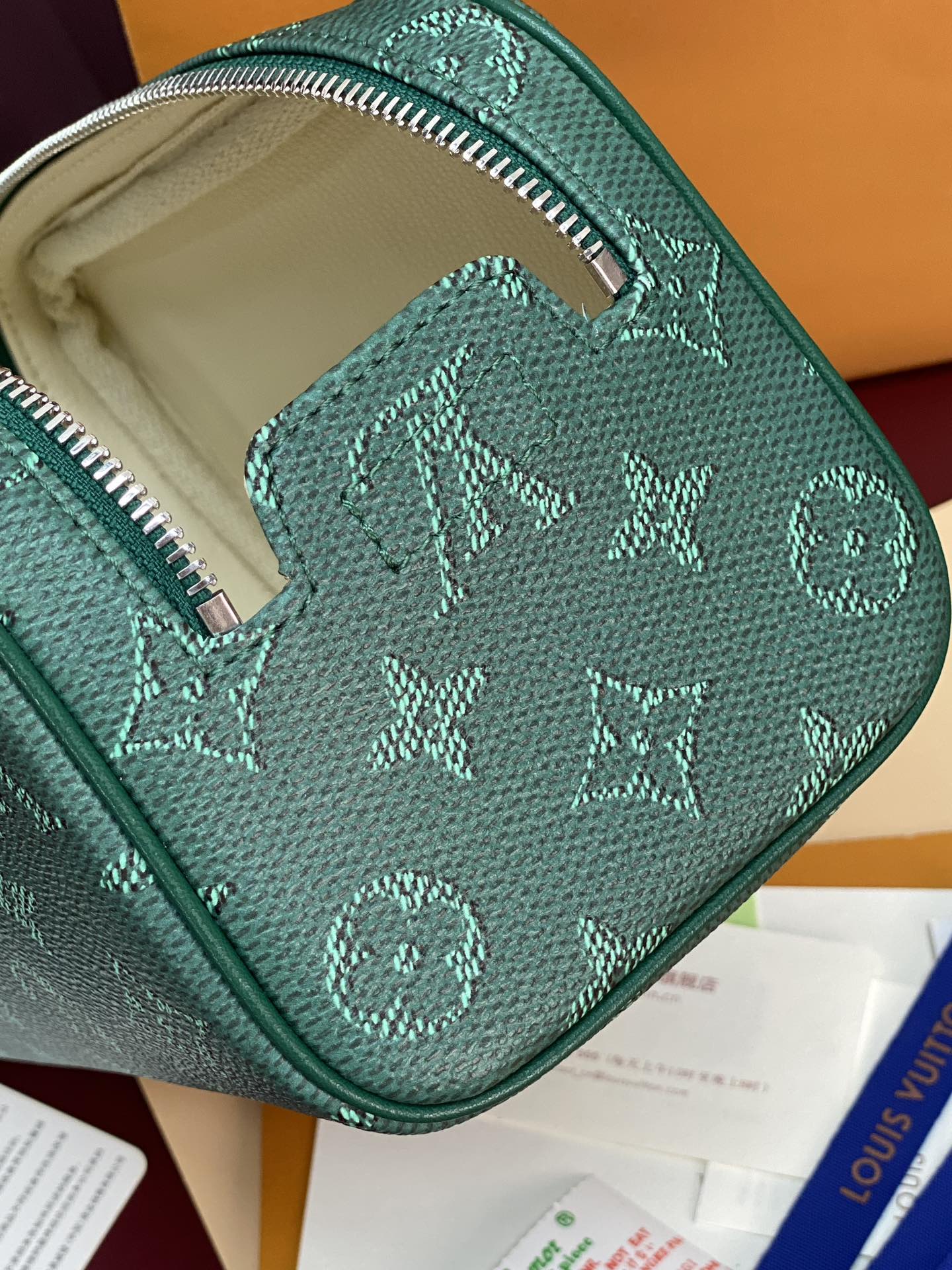 Green monogram bag opening with beige lining and zipper closure visible.