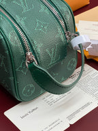 Green monogram crossbody bag with attached wrist strap and front zipper pull.