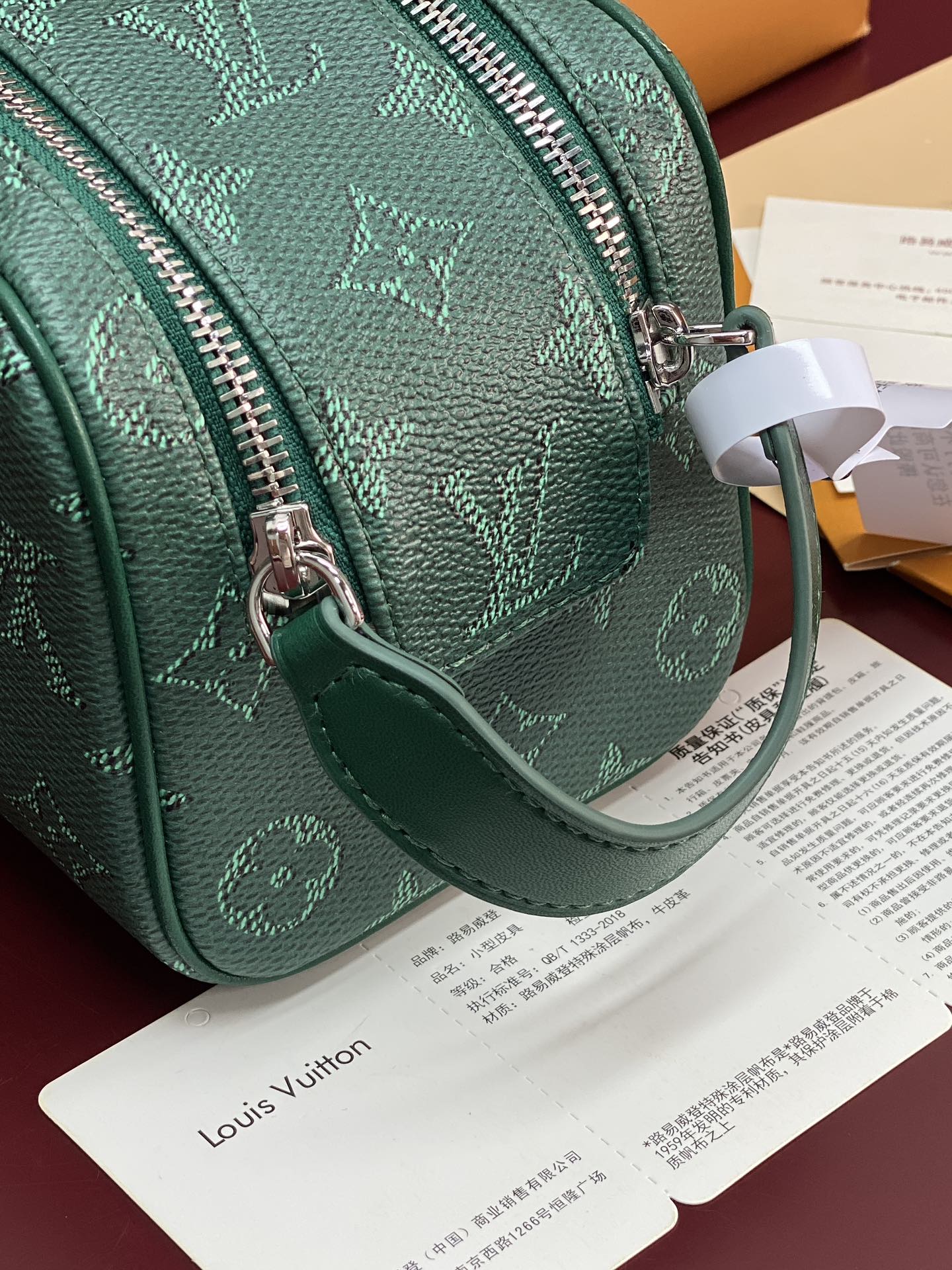 Green monogram crossbody bag with attached wrist strap and front zipper pull.