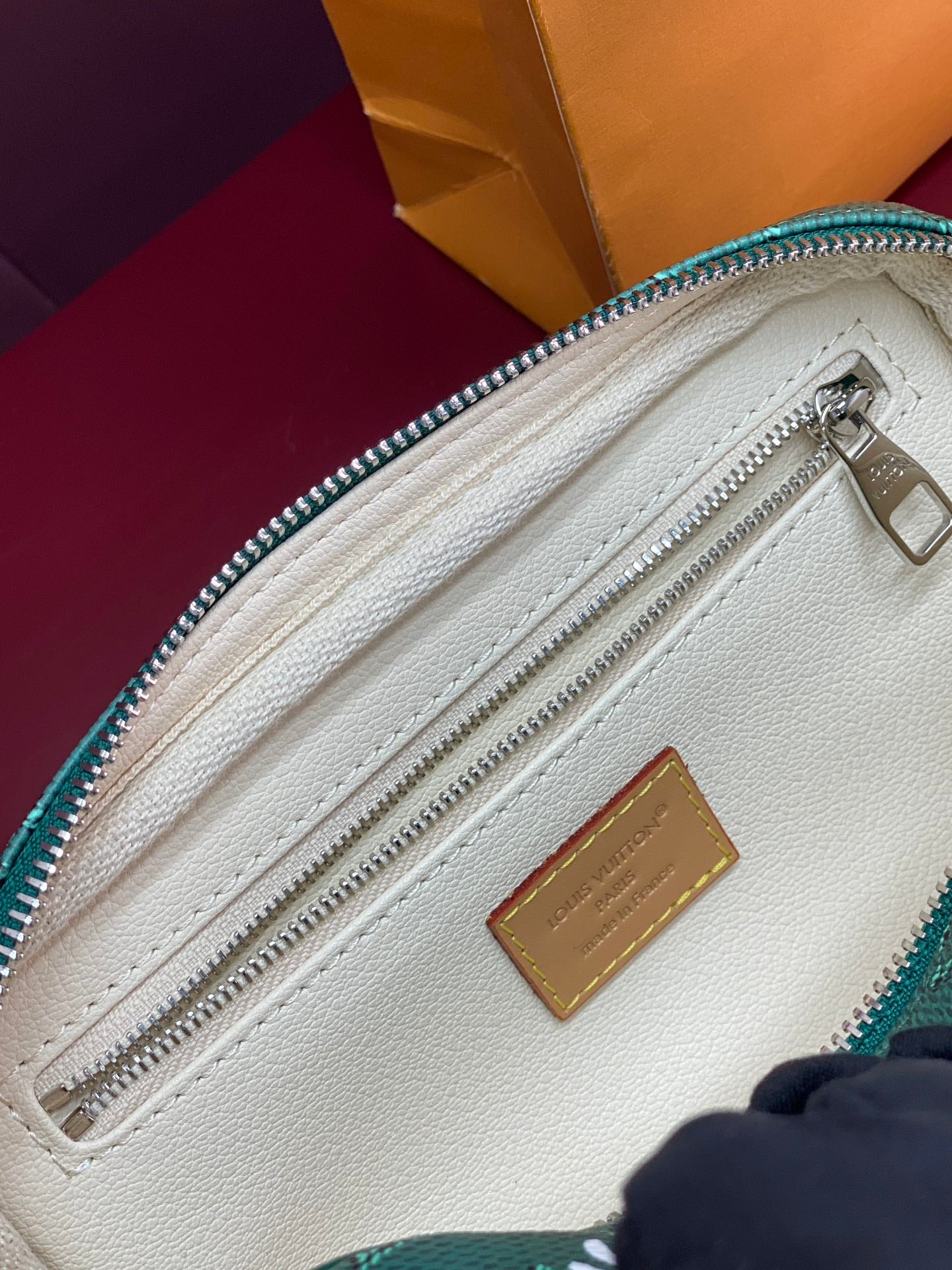 Beige interior of green monogram bag with zip track and leather patch.