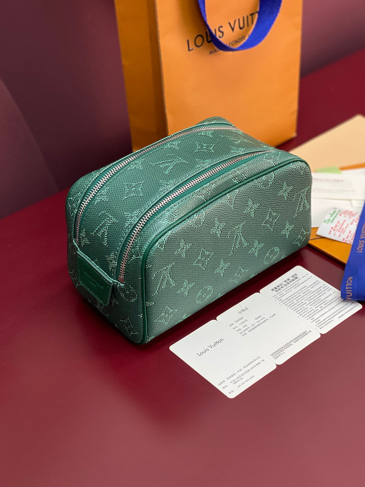 Green monogram vanity bag with curved silhouette and zip closure.