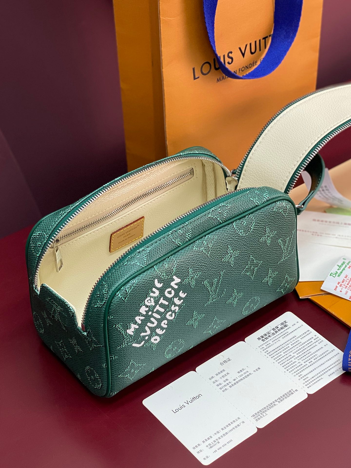 Green monogram toiletry bag shown open with beige interior and zipper.