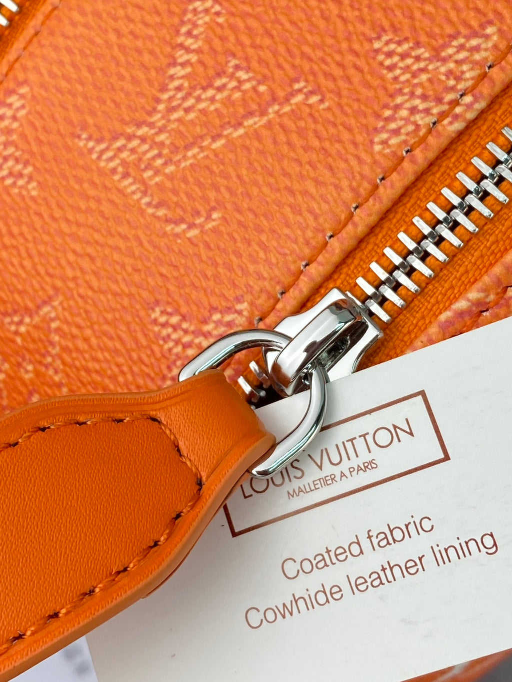 Orange monogram zip bag detail with shiny metal zipper and leather pull tab
