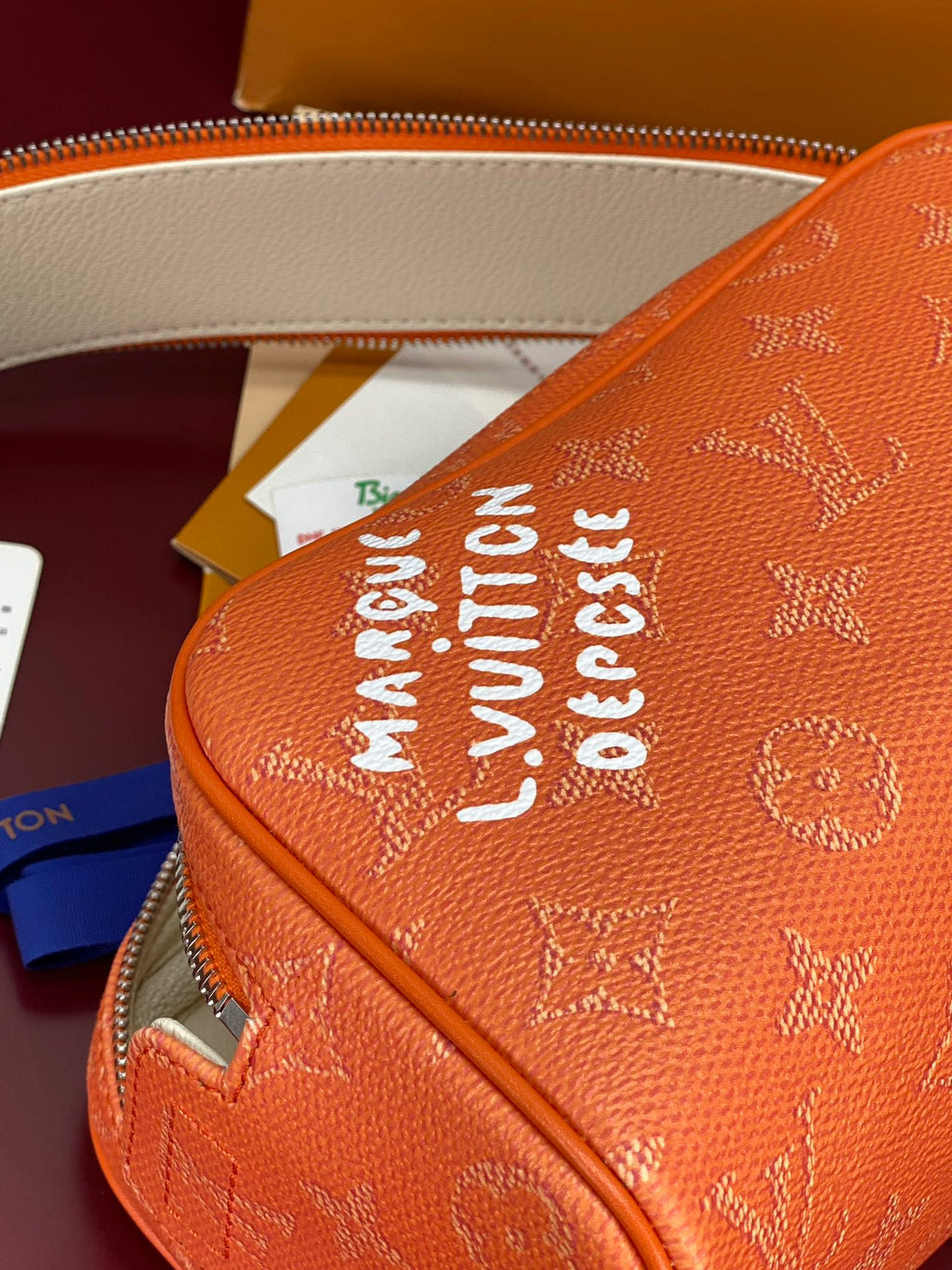 Orange monogram toiletry bag side with bold printed text near the zipper