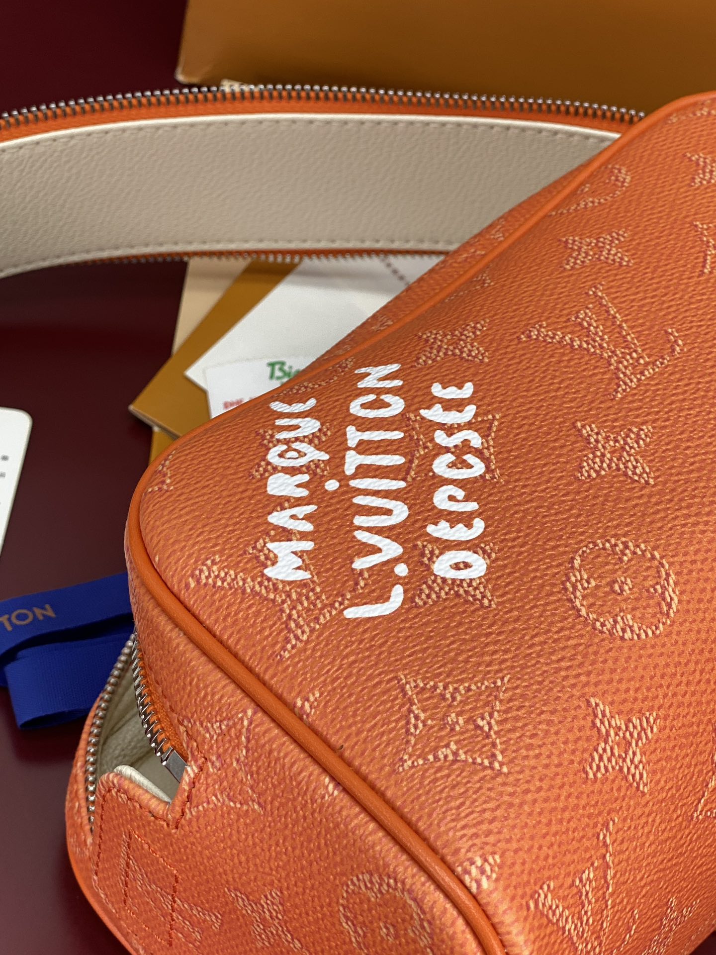 Orange monogram toiletry bag side with bold printed text near the zipper