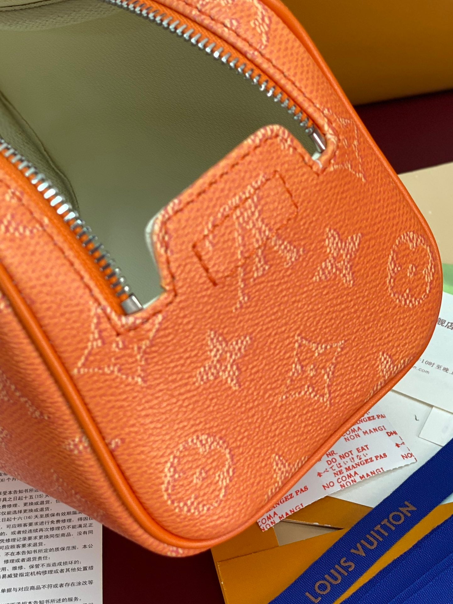 Orange monogram toiletry bag corner close-up with stitched leather and silver zipper