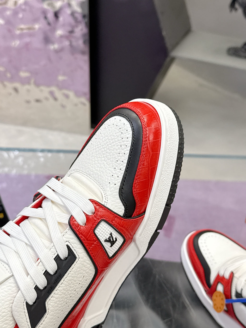 Side view of white and red Louis Vuitton sneaker with black panel and lace-up details
