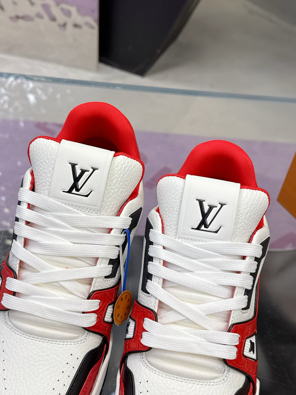 Close-up of white Louis Vuitton sneakers with red lining, lace-up, and LV logo on tongue