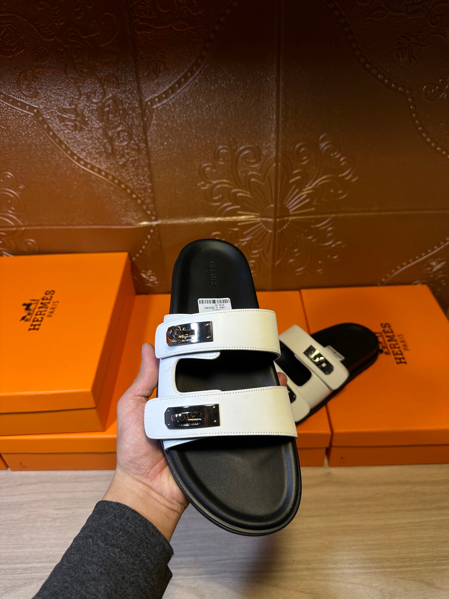 Hermes sandals held up, showing white straps and metal buckles on black footbed.