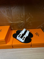 Hermes two-strap sandals, white straps on black footbed with metal buckle accents.