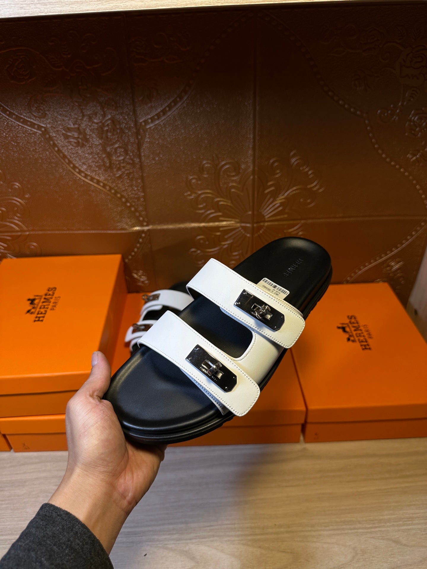 Hermes slide sandals held with white double straps and black sole, close angle.