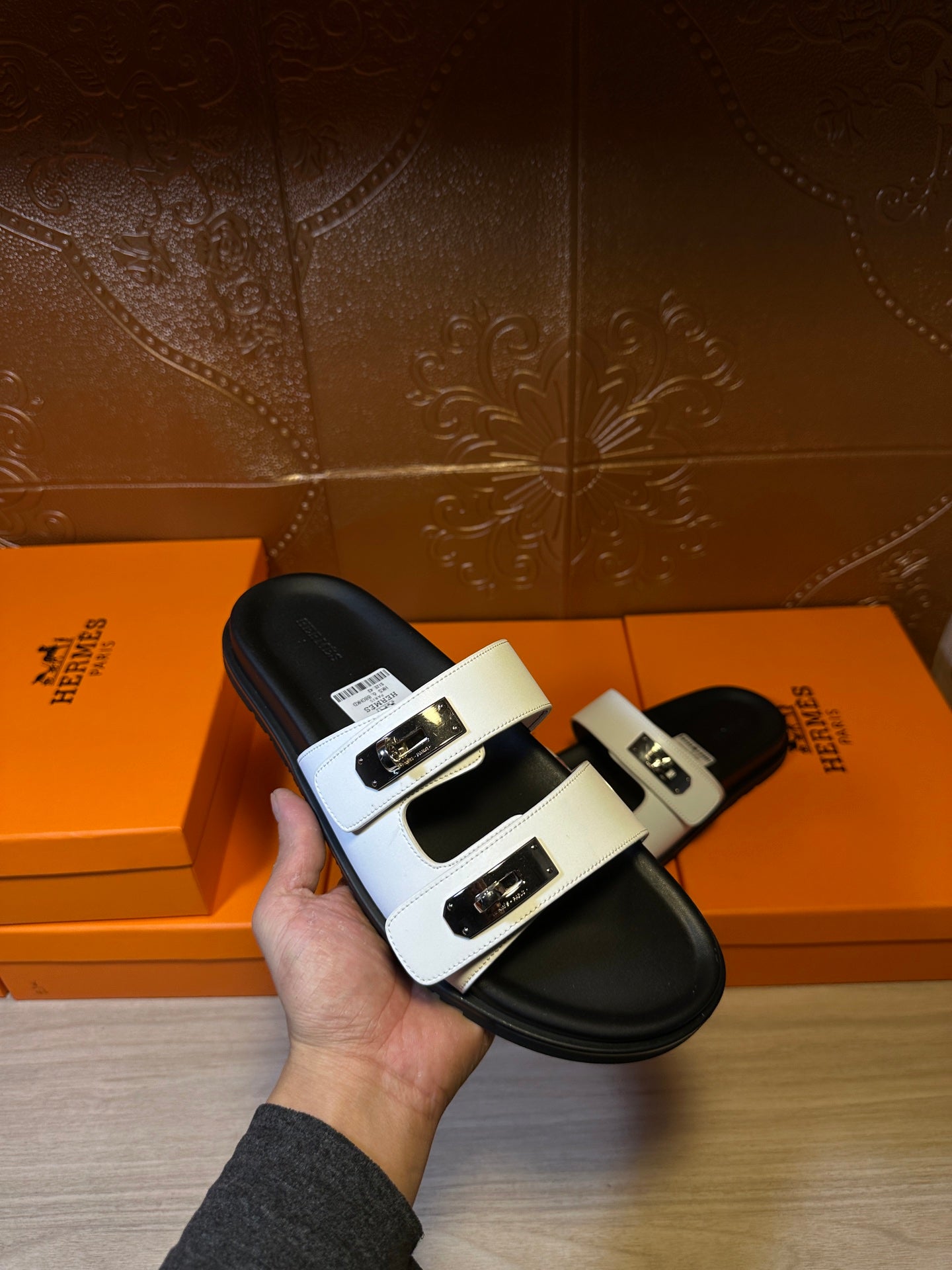 Hermes slide sandals in hand: white straps with metal buckle detail, black footbed.