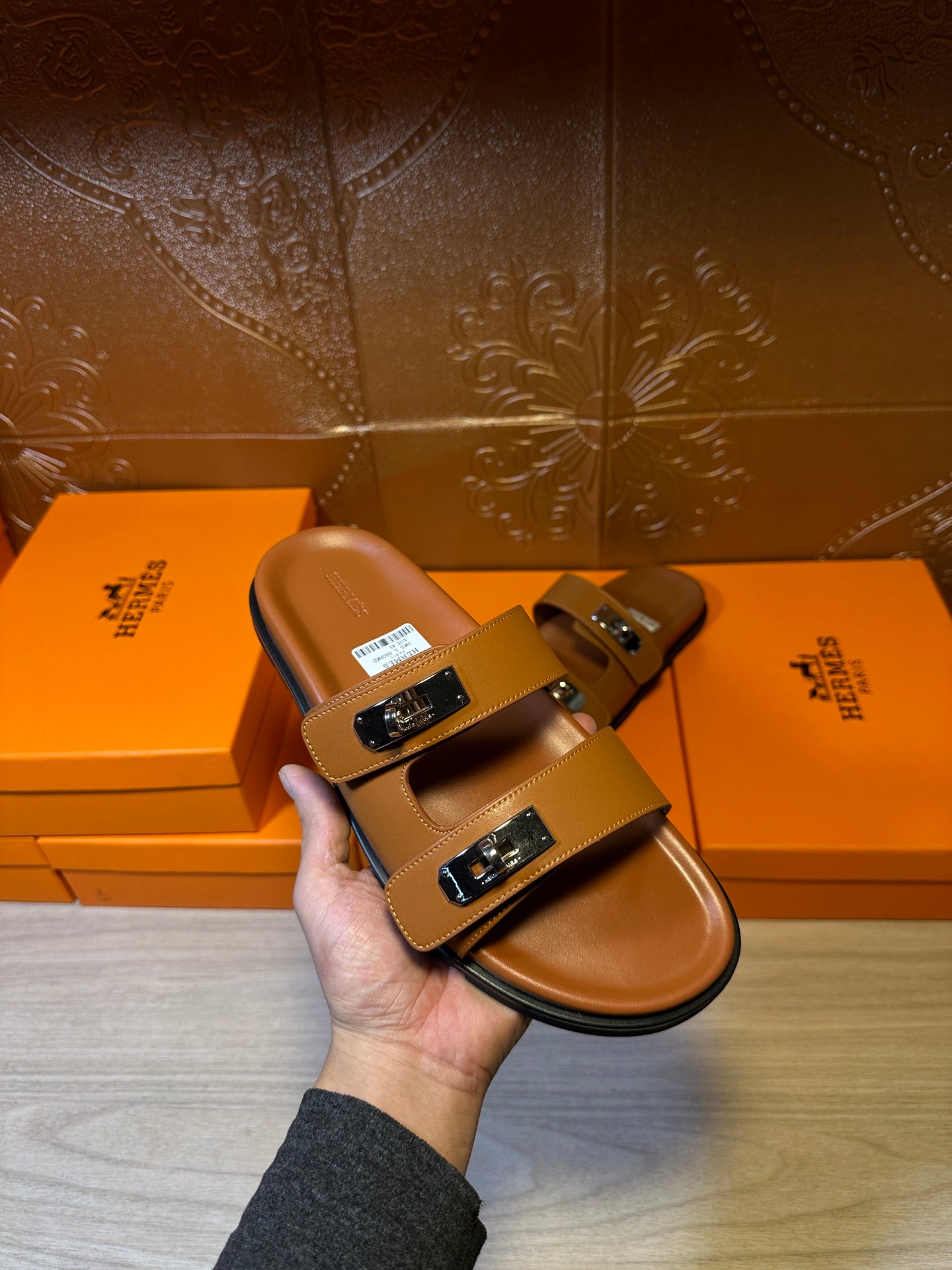 Hermes tan slide sandals held in hand, two straps with silver-tone buckles