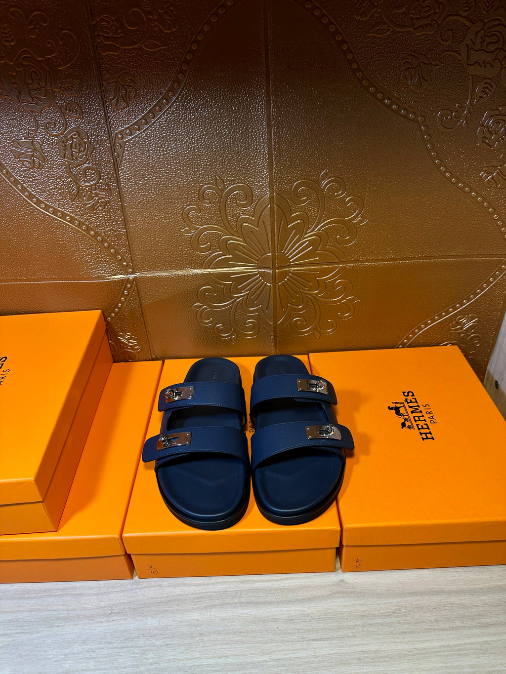 Hermes blue slide sandals with two front buckles, side-by-side on boxes