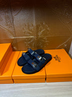 Hermes blue slide sandals with two front buckles, angled view on display