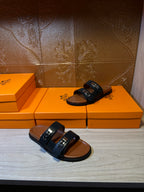 Pair of black slide sandals with two straps and silver buckles on tan soles
