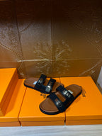 Black leather sandals with double straps and silver buckles over tan footbed