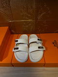 Hermes slide sandals with white upper, two wide straps, and metal buckles