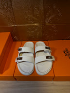 Hermes slide sandals with white upper, two wide straps, and metal buckles