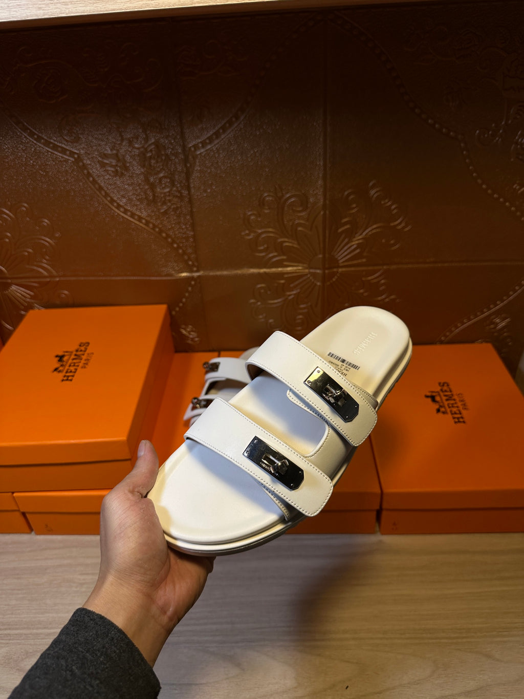 Hermes white sandals held by hand; two straps with metal buckle hardware