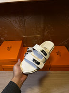 Hermes white sandals held by hand; two straps with metal buckle hardware