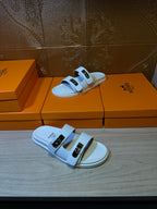 Hermes white sandals on display; two wide straps with metal buckle details