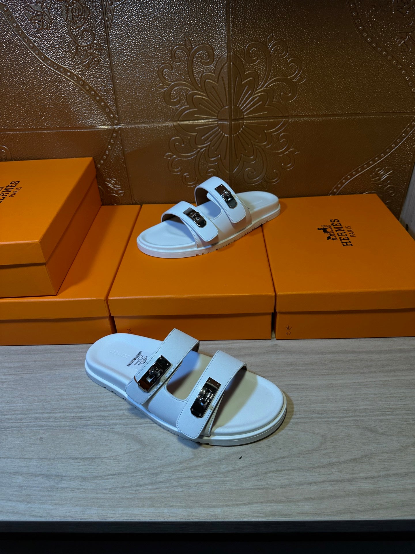 Hermes white sandals on display; two wide straps with metal buckle details