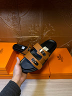 Tan-strap black slide sandals held in hand, with silver buckle detail