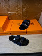 Hermes luxury sandals resting on a surface, navy straps with silver buckle hardware.