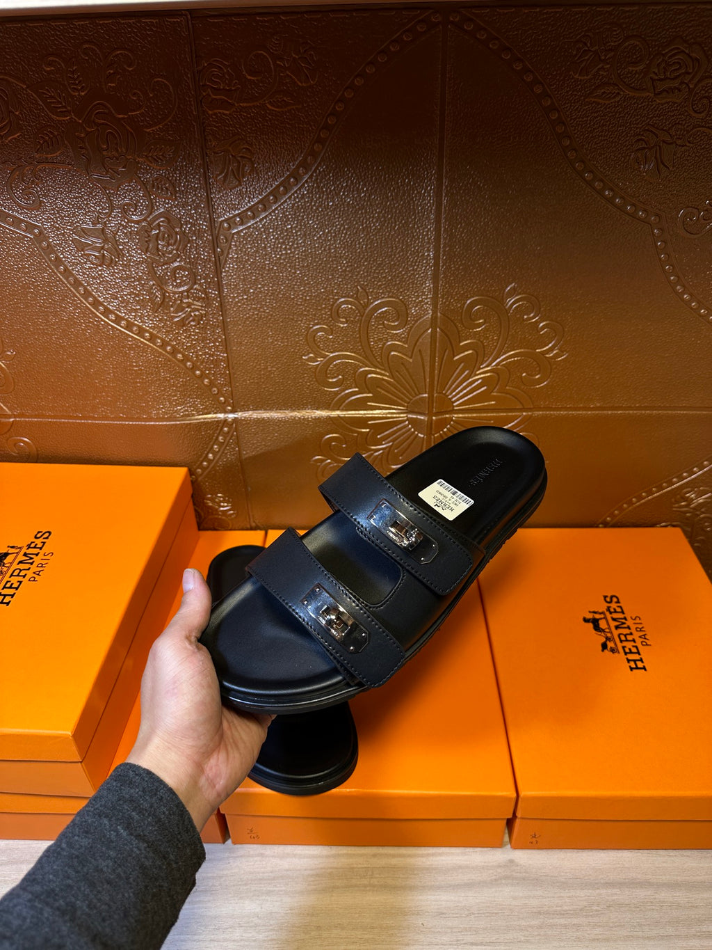 Black slide sandals with two buckled straps and thick flat sole, held up.