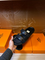Black slide sandals with two buckled straps and thick flat sole, held up.
