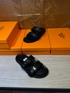 Black sandals angled view, two wide straps with shiny metal buckles and flat sole.
