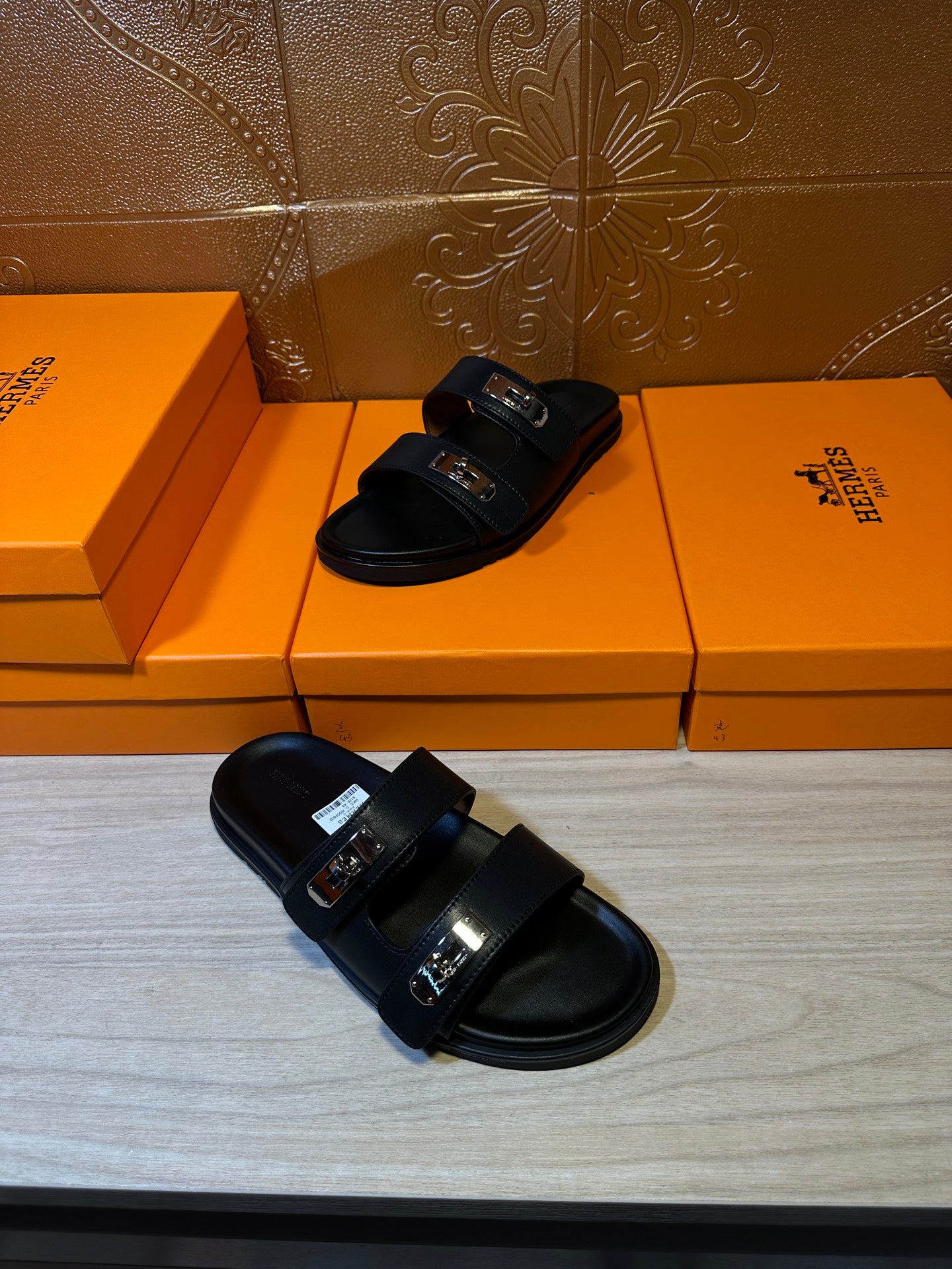 Black sandals angled view, two wide straps with shiny metal buckles and flat sole.