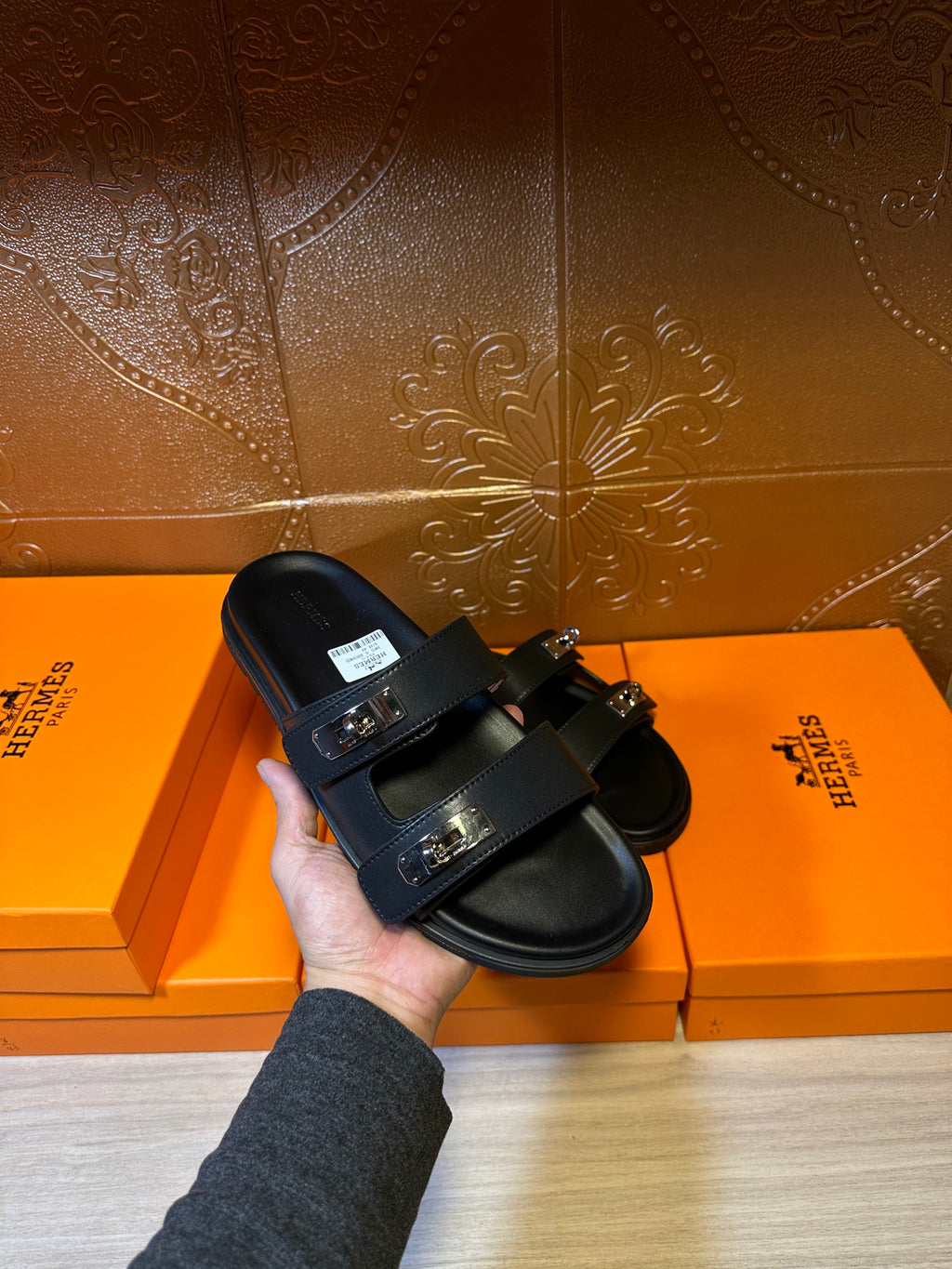 Black sandals with wide strap buckles and flat sole, shown held in hand.