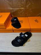 Black sandals, side view, with two straps and metal buckle at the instep.