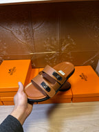 Tan slide sandals with double straps and silver buckles, held in hand