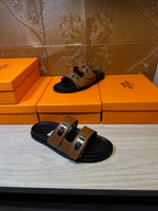 Pair of tan slide sandals with black footbed, two buckle straps, and silver metal hardware
