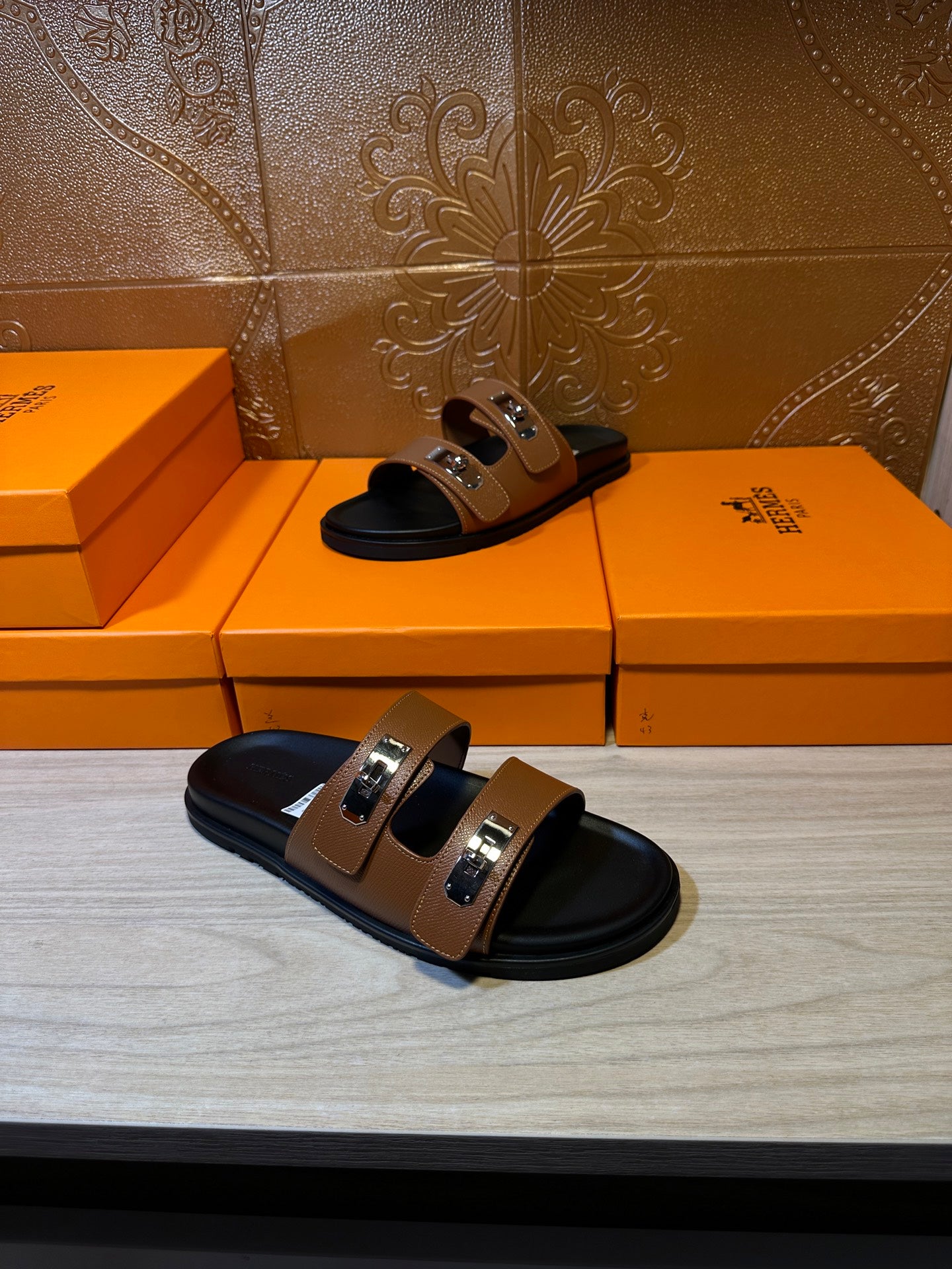Pair of tan slide sandals with black footbed, two buckle straps, and silver metal hardware