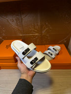 White Hermes slide sandals shown front, double straps with silver buckle detail