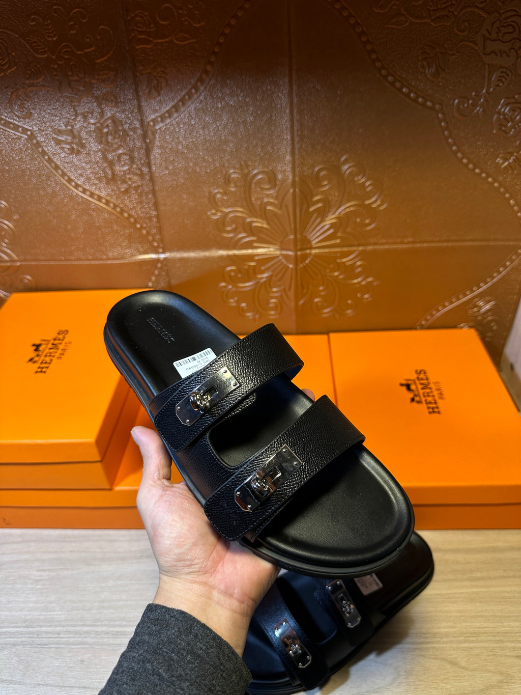 Hermes black leather sandals held in hand, double straps with metal buckles