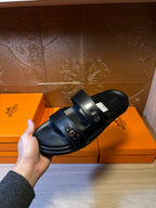 Hermes black leather sandals held in hand, close-up of double buckle straps