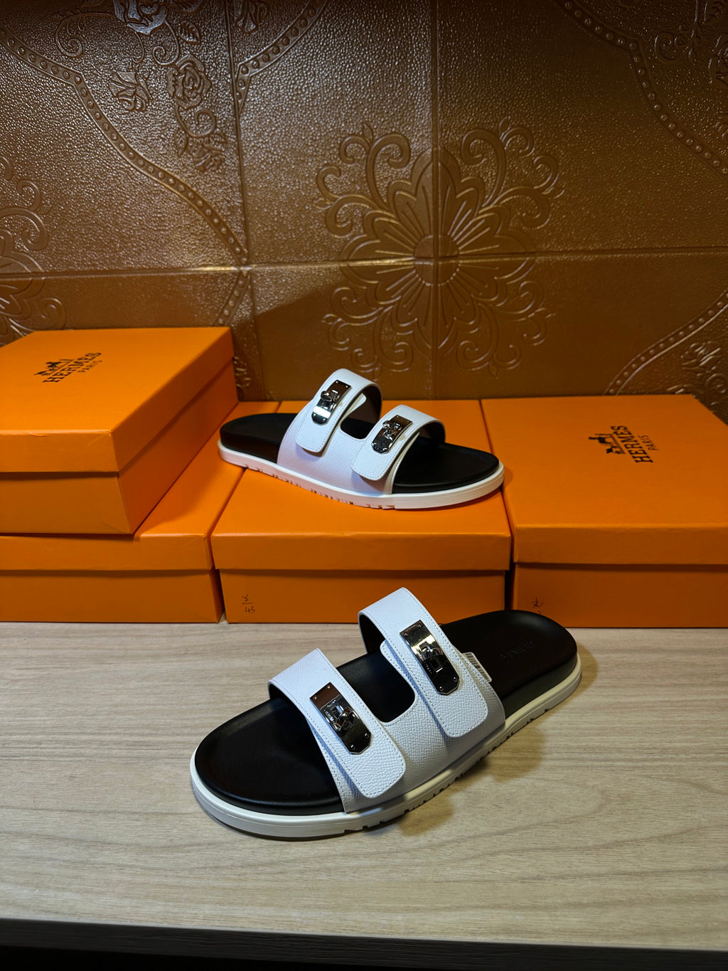 Hermes slide sandals on display, white straps with gold buckles and black footbeds