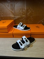 Hermes slide sandals on display, white straps with gold buckles and black footbeds