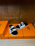 Hermes slide sandals set on orange boxes, white straps with gold buckles and black footbeds