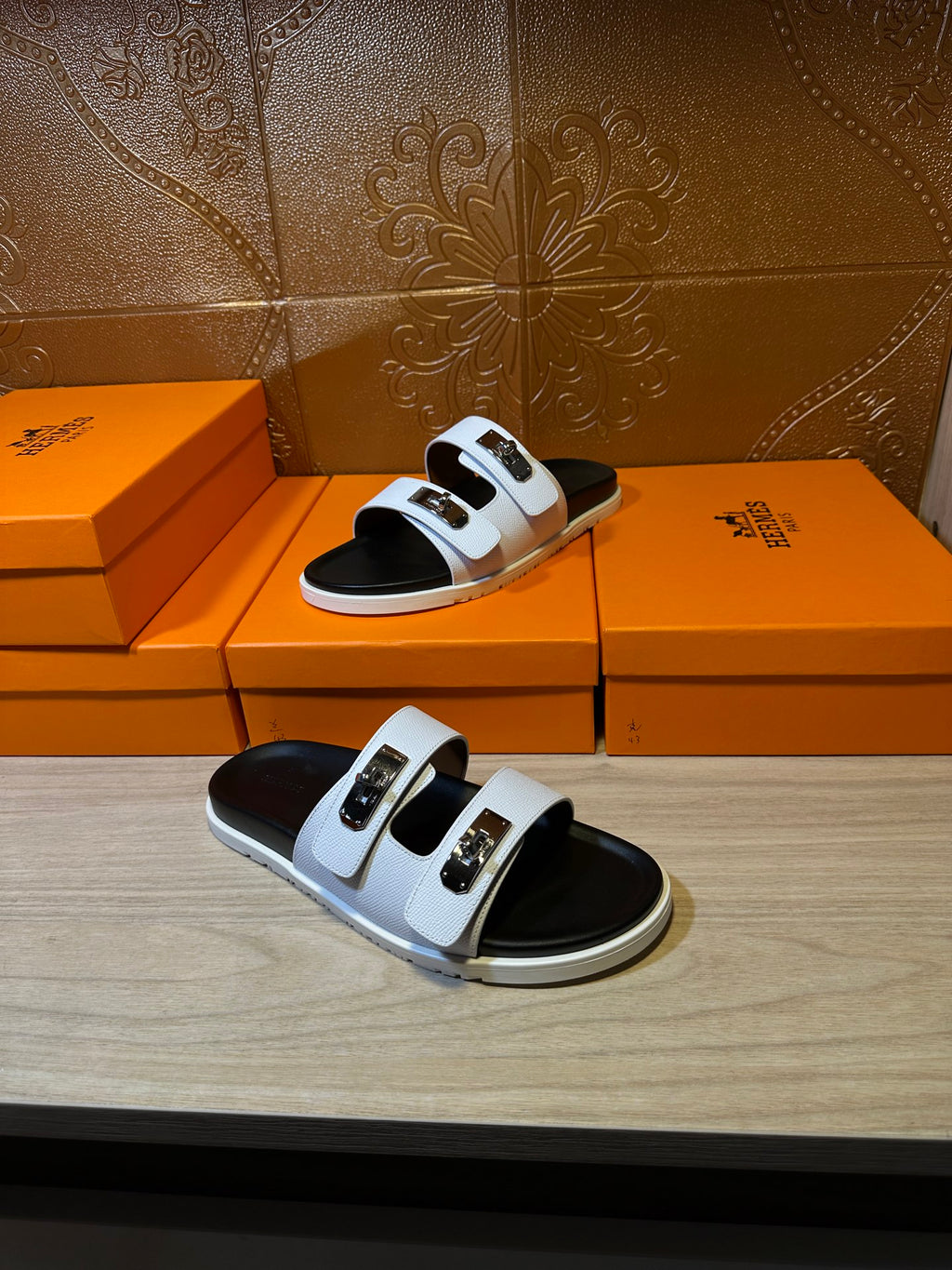 Hermes slide sandals on boxes, one sandal visible with white straps and gold buckles