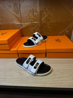 Hermes slide sandals on boxes, one sandal visible with white straps and gold buckles