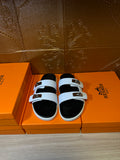 Hermes slide sandals with white straps, black footbeds, and gold buckles