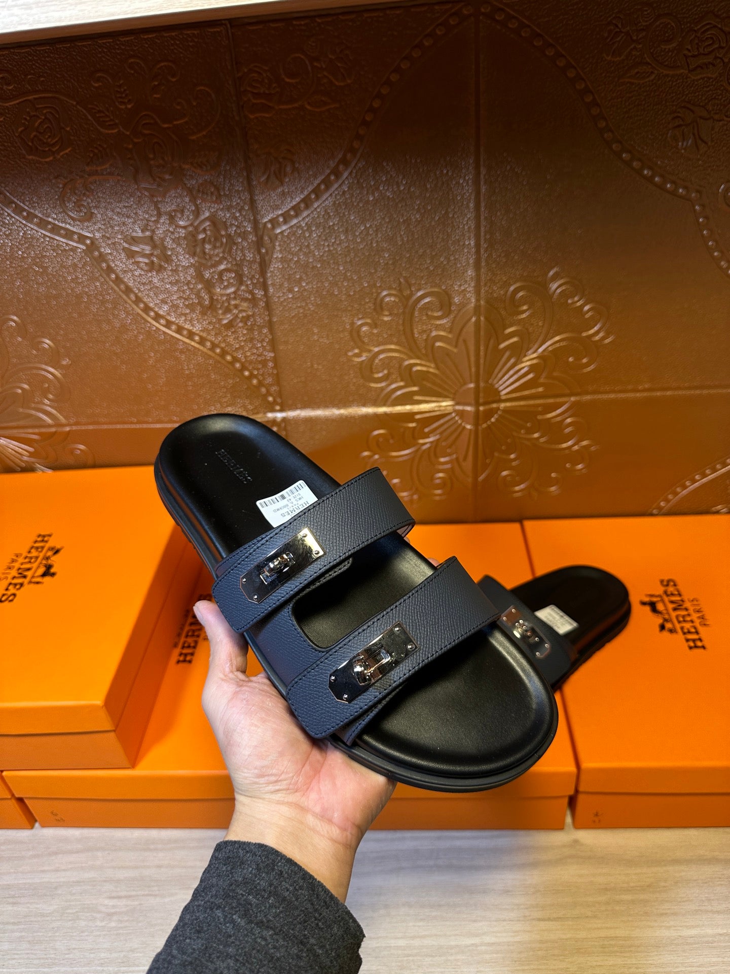 Hand holding Hermes blue leather slide sandal with silver buckle straps