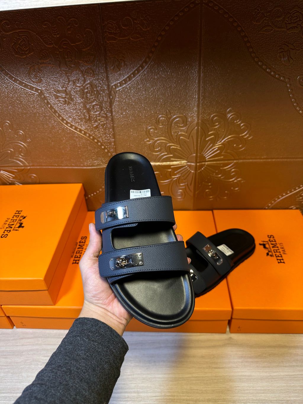 Hermes blue slide sandal held upright, black footbed and double buckles